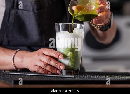 Femme Bartender versant du thé Matcha dans Un verre avec du lait et de la glace, avec Un gros plan de la main Banque D'Images
