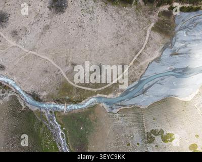 Vue aérienne d'un drone d'une rivière glaciaire tressée qui coule sur un lit pierreux à côté de pistes de terre sur une plaine de montagne sèche Banque D'Images