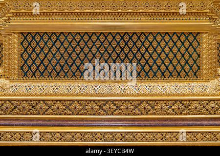 Un fond décoratif thaïlandais complexe présente des motifs floraux en mosaïque de verre en bleu et vert, rehaussés par des détails dorés horizontaux superposés pour un prem Banque D'Images