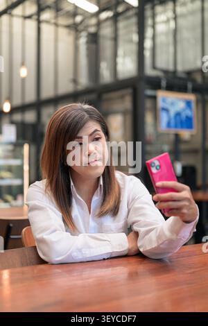Portrait de style de vie heureux d'une femme transgenre Isan d'Asie du Sud-est dans ses années 40 doucement souriant tout en prenant selfie avec téléphone à une table de restaurant. T Banque D'Images
