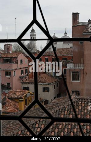 Vue sur les toits en terre cuite de Venise encadrés par une fenêtre gothique à l'intérieur du Palais des Doges (Palazzo Ducale), avec les dômes et le clocher du Banque D'Images