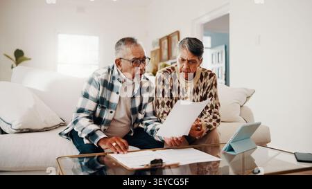 Documents, confus et couple senior sur canapé à la maison avec fonds de retraite, épargne ou budget. Revue, paperasse et homme âgé avec femme pour Banque D'Images
