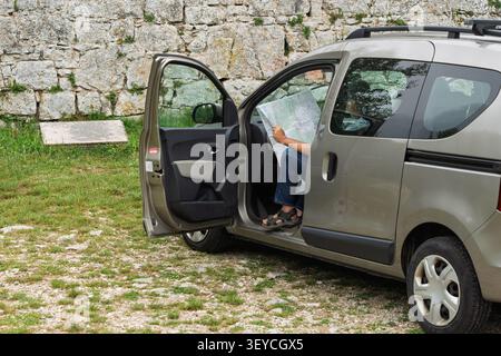 Homme lisant la carte, dans la zone rurale avec mur de pierre et herbe, avec voiture, carte, avec pierre, métal, texture du papier, vue de côté, avec vert, g. Banque D'Images