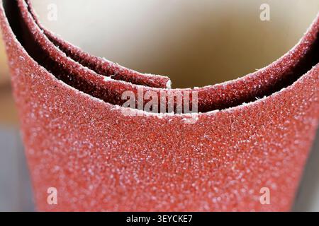 Un gros plan de papier abrasif rouge roulé avec texture rugueuse et grain fin pour poncer et polir les surfaces Banque D'Images