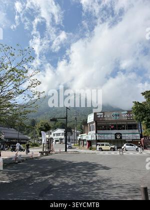 Rue commerçante au bord de la route dans une ville de montagne japonaise, avec des restaurants locaux et des enseignes de magasins en caractères japonais, des collines verdoyantes et des dramati Banque D'Images