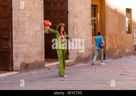 Une jeune femme portant une couronne de laurier italienne traditionnelle et tenant des fleurs célèbre la remise des diplômes dans une rue du centre historique de Sienne, en Toscane Banque D'Images