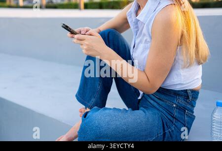 Jeune femme vérifiant le téléphone sur les marches extérieures bleues à la lumière du jour Banque D'Images