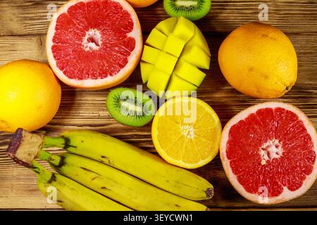 Assortiment de fruits tropicaux sur table en bois. Nature morte avec bananes, mangues, oranges, pamplemousses et kiwis Banque D'Images