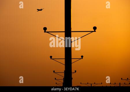 Avion silhouette survolant la piste de l'aéroport au coucher du soleil Banque D'Images