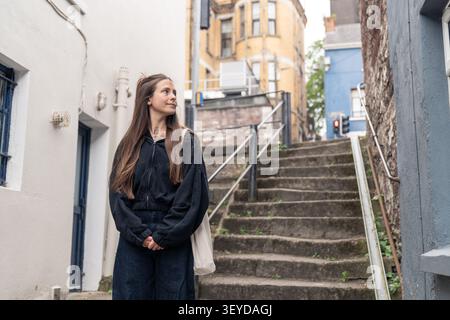 Jeune femme explorant une ruelle urbaine, regardant autour de lui Banque D'Images