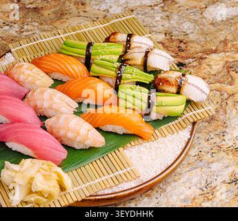 Un plateau vibrant de sushis présente des pièces colorées comprenant du saumon, des crevettes et de l'anguille. Le plat est habilement disposé sur un tapis de bambou, entouré de gingembre et de wasabi. Banque D'Images