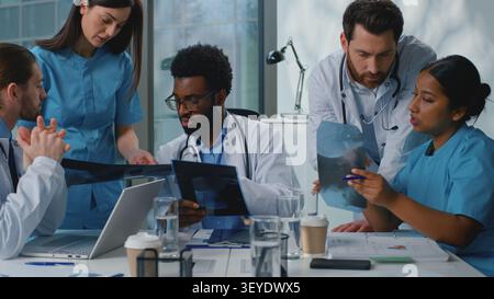 Équipe de médecine internationale analysant le cancer des poumons par rayons X diagnostic de pandémie covid partenariat parlant dans une clinique moderne. Multiracial cinq médecins parlent Banque D'Images