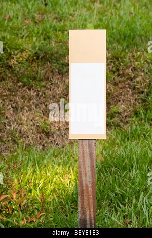 Un panneau rectangulaire blanc minimaliste monté sur un poteau en bois se dresse dans un paysage herbeux, offrant un espace de copie pour les directions Banque D'Images