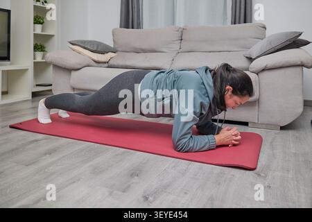 Femme effectuant une planche d'avant-bras pendant une séance de fitness à domicile sur un tapis de yoga, en se concentrant sur la stabilité et la force du tronc. Banque D'Images