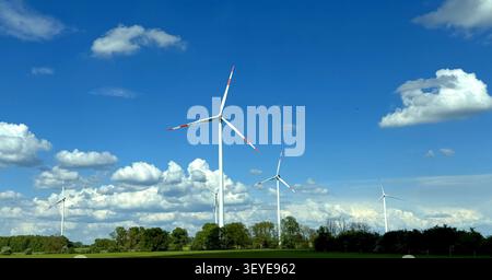 Cinq grandes éoliennes sur un champ vert sous un ciel bleu avec des nuages dispersés, mettant en valeur la production d'énergie renouvelable dans un paysage rural Banque D'Images