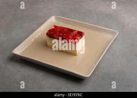 Tranche de cheesecake à la fraise sur plaque en céramique avec fond gris rustique Banque D'Images
