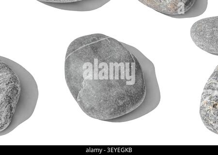 Vue de dessus d'un arrangement de galets gris isolé sur fond blanc. Composition organique minimaliste avec des ombres douces et une texture rocheuse détaillée Banque D'Images