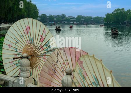 Une vue d'un étang avec des bateaux à Pékin, avec des parapluies traditionnels chinois en papier au premier plan Banque D'Images