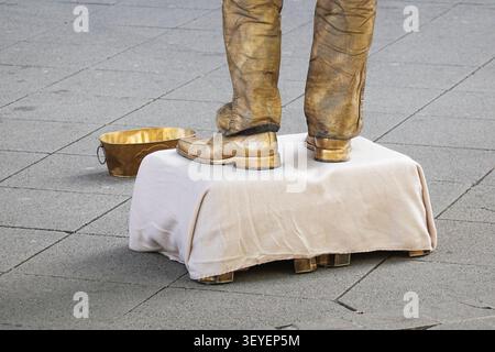 Statue vivante artiste de rue peint en or se produit sur la rue de la ville avec seau doré Banque D'Images