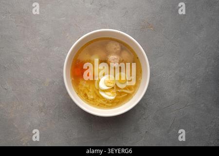 Bol à soupe maison clair avec des œufs, des boulettes de viande, des nouilles, des légumes sur la surface de pierre Banque D'Images