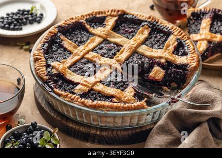 Tarte aux myrtilles avec croûte en treillis tranchée sur un fond de table texturé brun, dessert traditionnel fait maison Banque D'Images