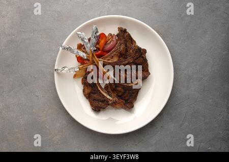 Côtelettes d'agneau grillées avec légumes rôtis sur assiette blanche sur pierre grise Banque D'Images