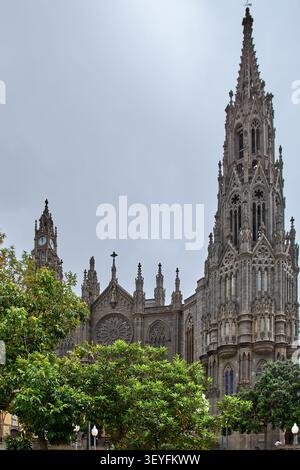 Magnifique architecture néo-gothique de la cathédrale encadrée par le feuillage verdoyant vibrant du parc, mettant en valeur les monuments historiques européens, le tourisme culturel et le patrimoine Banque D'Images