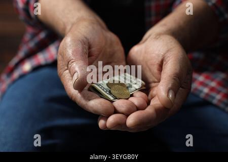 Pauvreté. Homme senior sans abri avec un billet de banque en dollars et des pièces à l'intérieur, gros plan Banque D'Images