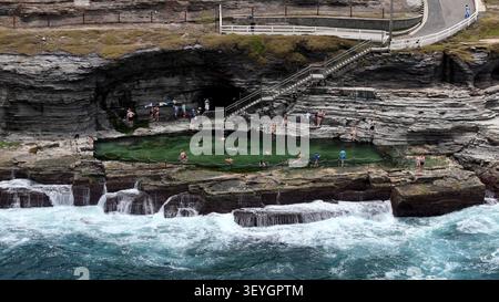 Vue aérienne de la piscine océanique de Bogey Hole avec des gens nageant dans l'eau verte claire, entouré de formations rocheuses accidentées et de vagues écrasantes à New Banque D'Images