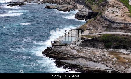 Vue aérienne de la piscine océanique historique de Bogey Hole creusée dans la côte rocheuse avec des vagues s'écrasant contre les falaises et les gens nageant dans la wa Banque D'Images