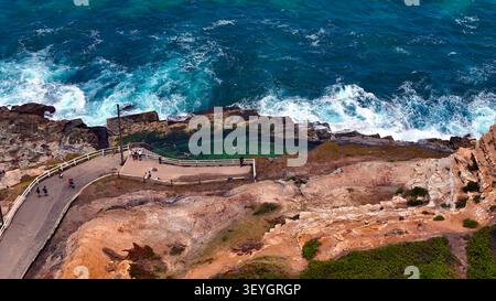 Vue aérienne de la piscine océanique de Bogey Hole avec des gens nageant et marchant le long du sentier côtier, entouré de falaises accidentées et de l'océan Pacifique Banque D'Images