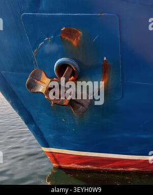 Ancre de navire rouillée montée sur la proue d'un navire peint en bleu au-dessus de la mer Méditerranée turquoise, en Grèce. Banque D'Images