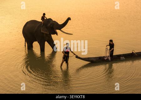 Lien son Lak, Vietnam - 07 avril 2026 : vue aérienne d'un éléphant avec un cavalier, un homme debout dans l'eau et une femme pêchant depuis un bateau en bois Banque D'Images