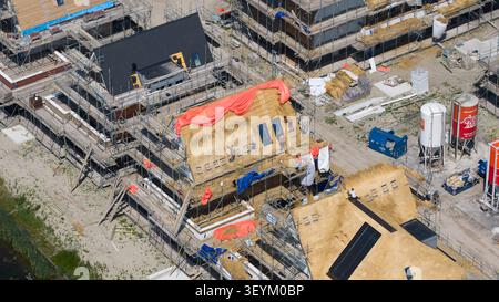 Weesp, Noord-Holland, pays-Bas - 16 juin 2026 : vue aérienne d'ouvriers de la construction installant des toits de chaume sur des maisons neuves entourées d'échafaudages Banque D'Images