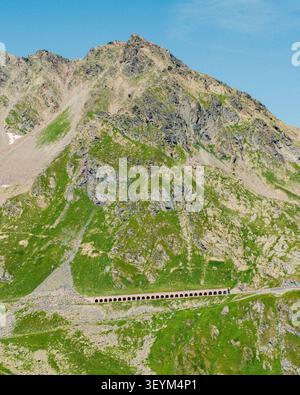 Vue aérienne du col du Grand Saint-Bernard avec sa galerie de pierres historique nichée contre les montagnes alpines accidentées sous un ciel bleu clair à Saint Banque D'Images