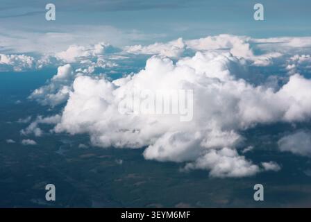 La vue aérienne à couper le souffle capture des cumulus tourbillonnants dérivant au-dessus d'un patchwork de terre verte loin en dessous, encadré par un vaste ciel bleu serein Banque D'Images