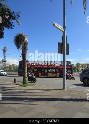 Barcelone, Espagne - 18 juillet 2022 la vue lumineuse de la rue de midi montre un bus touristique rouge à deux étages, des scooters, des palmiers, la circulation et la grande tour agai Banque D'Images