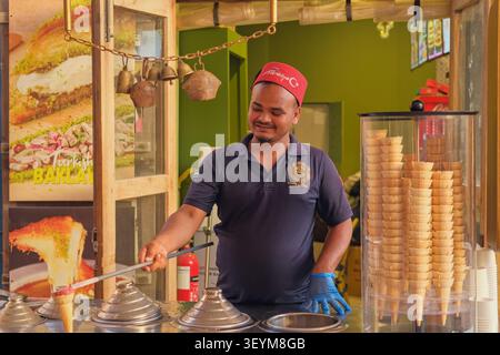 Dubai, Émirats arabes unis,20.06.2026 Un vendeur turc de glaces sert du dondurma traditionnel dans une boutique de desserts, préparant des glaces artisanales dans des cônes gaufrés pour les touristes. Banque D'Images