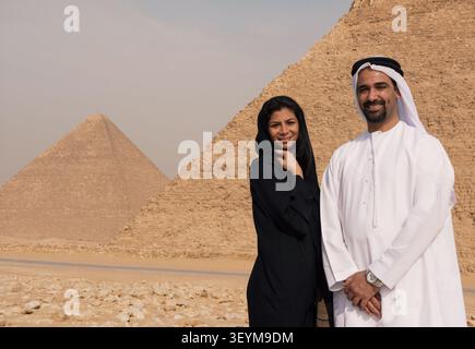 Couple émirati romantique en abaya traditionnelle et kandura blanc souriant chaleureusement ensemble devant les pyramides emblématiques de Gizeh idéales pour les couples MENA Banque D'Images