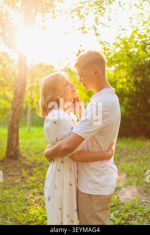 Un moment romantique capturé entre un jeune homme et une jeune femme, baigné dans la lueur chaude de la lumière du coucher du soleil au milieu d'une végétation luxuriante Banque D'Images