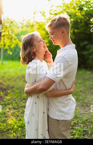 Un jeune couple joyeux partage un moment d'amour en plein air, baigné dans la lueur chaude du soleil couchant, entouré d'une végétation luxuriante Banque D'Images