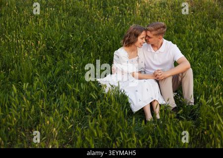 Un couple romantique profite d'un après-midi paisible en plein air, niché ensemble au milieu de hautes herbes et de fleurs sauvages Banque D'Images