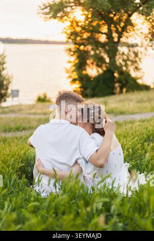 Un moment romantique capturé alors qu'un couple partage une tendre étreinte au milieu d'une grande herbe verte avec le coucher du soleil derrière un arbre Banque D'Images