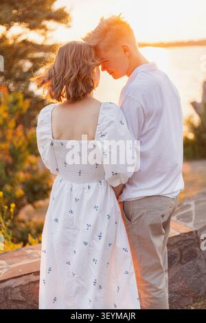 Un moment romantique capturé alors qu'un jeune couple partage une tendresse étreinte sur fond d'un coucher de soleil serein sur l'eau Banque D'Images