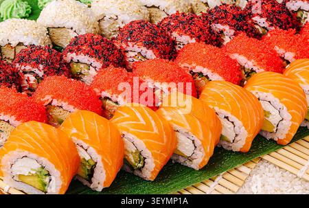 Un plateau vibrant présente un assortiment de rouleaux de sushi colorés, soigneusement arrangés. Les rouleaux comprennent du saumon, de l'avocat et des garnitures comme des œufs de poisson brillants, invitant les invités à se livrer. Banque D'Images
