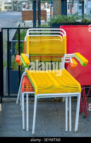 Le personnel du restaurant a empilé ces chaises multicolores vibrantes à l'extérieur pour dégager l'espace patio, signalant la fin du service et assurant la fourrure Banque D'Images