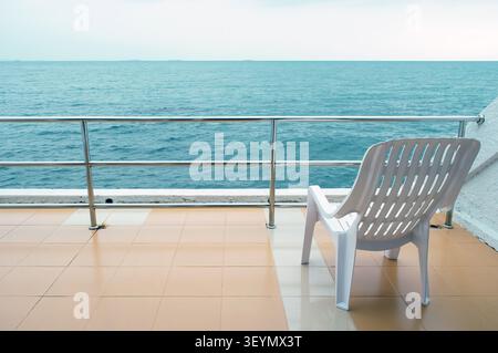une chaise en plastique se tient seul à la terrasse de l'hôtel en face de la mer ouverte avec un espace vide d'un côté Banque D'Images