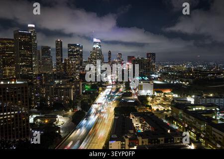 Vue aérienne nocturne sur Los Angeles avec ses gratte-ciel brillants, ses sentiers lumineux d'autoroute, ses nuages spectaculaires et son réseau urbain dense Banque D'Images