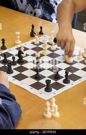 Enfants jouant une partie d'échecs sur une table en bois, avec un joueur faisant un mouvement. L'image représente l'apprentissage, la stratégie, la concentration, la logique Thi Banque D'Images