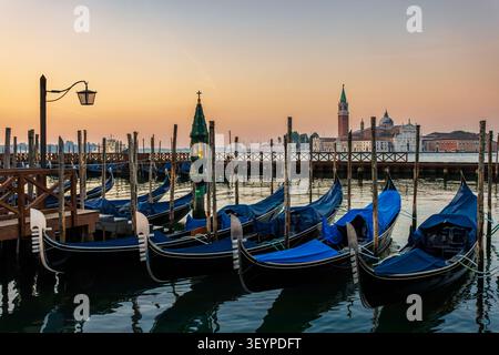Lever de soleil à l'embarcadère de Venise près de San Marco Plaza avec amarrage de gondole et San Giorgio Maggiore à travers le lagon sous un ciel chaud le 19 juin 2 Banque D'Images